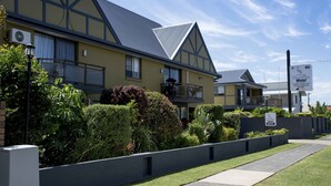 Un motel de dos pisos con balcón, un letrero que indica habitaciones disponibles y un césped bien cuidado.