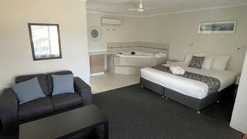 Een moderne slaapkamer met een bed, een bank, een klein tafeltje, een plafondventilator en een badkamer met een bad.