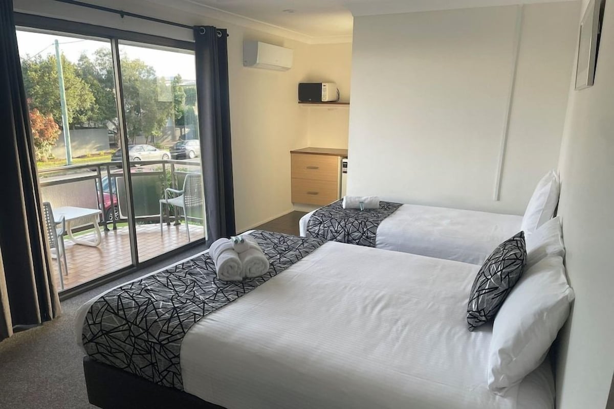 Habitación de hotel con dos camas, balcón, escritorio pequeño y microondas.
