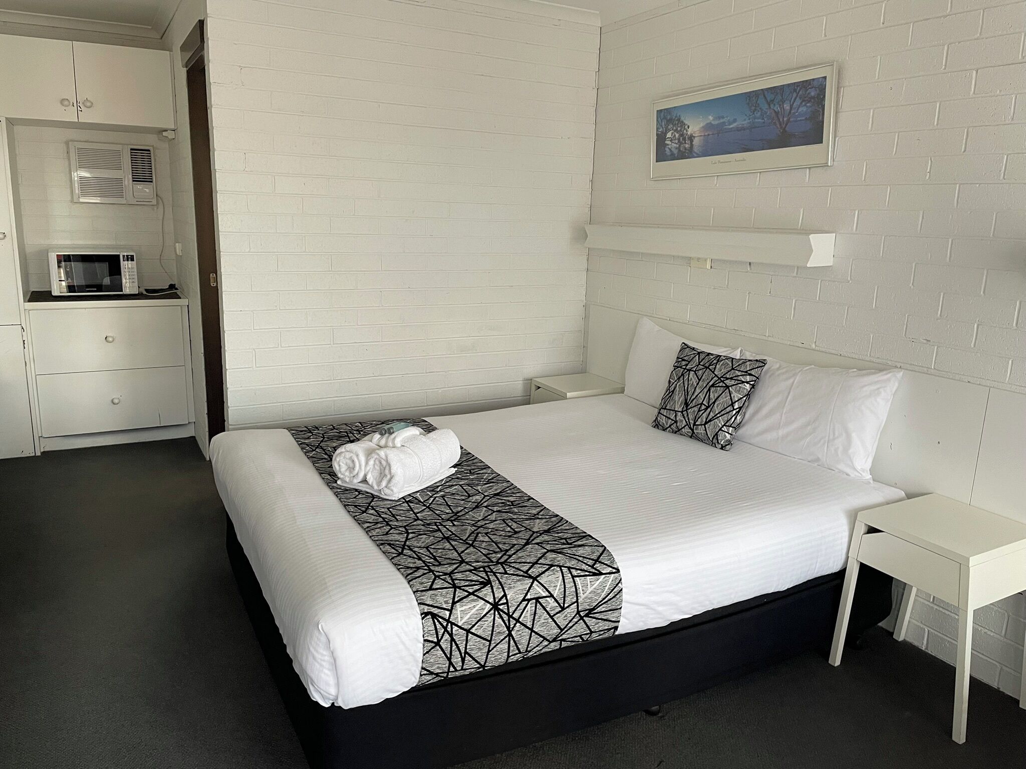 Ein Hotelzimmer mit einem Bett, einem Nachttisch, einem kleinen Tisch, einer Mikrowelle und einem Schrank.