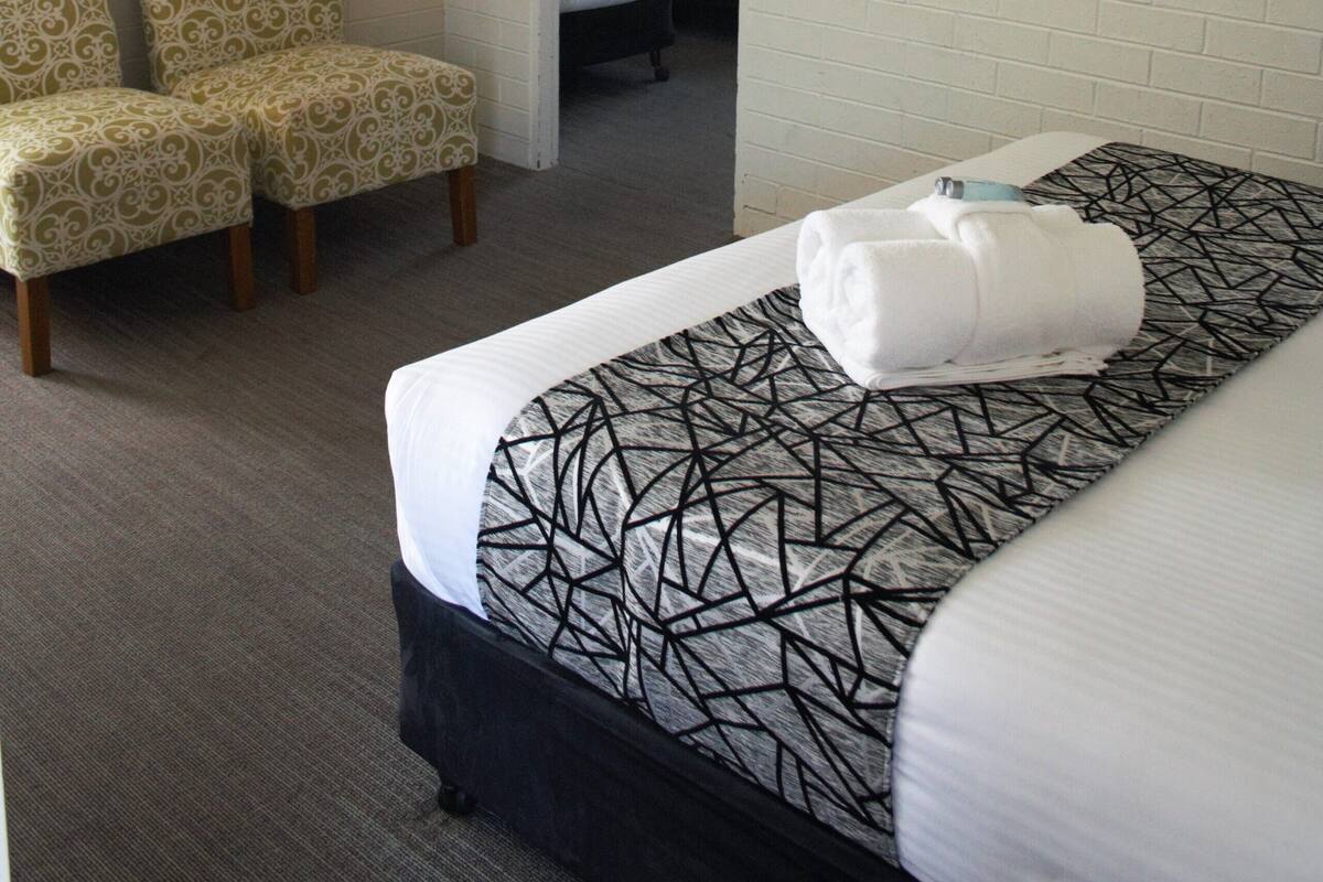 A hotel room with a bed, two patterned chairs, a television, and a painting of flowers.