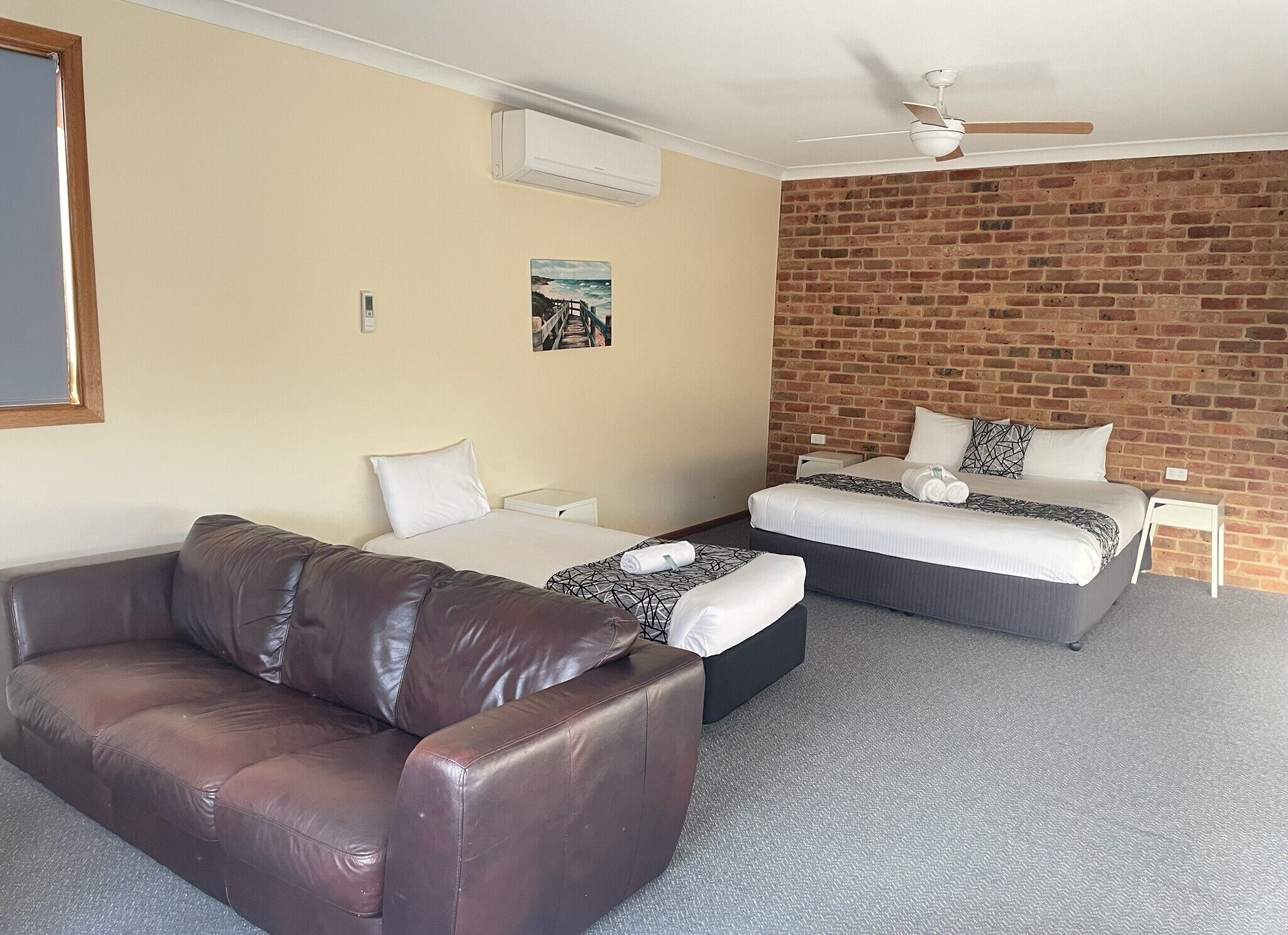 A hotel room with a brick wall, a ceiling fan, a bed, a sofa, and a painting on the wall.