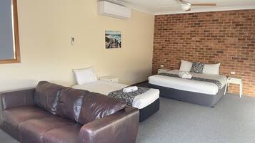 A hotel room with a brick wall, a ceiling fan, a bed, a sofa, and a painting on the wall.