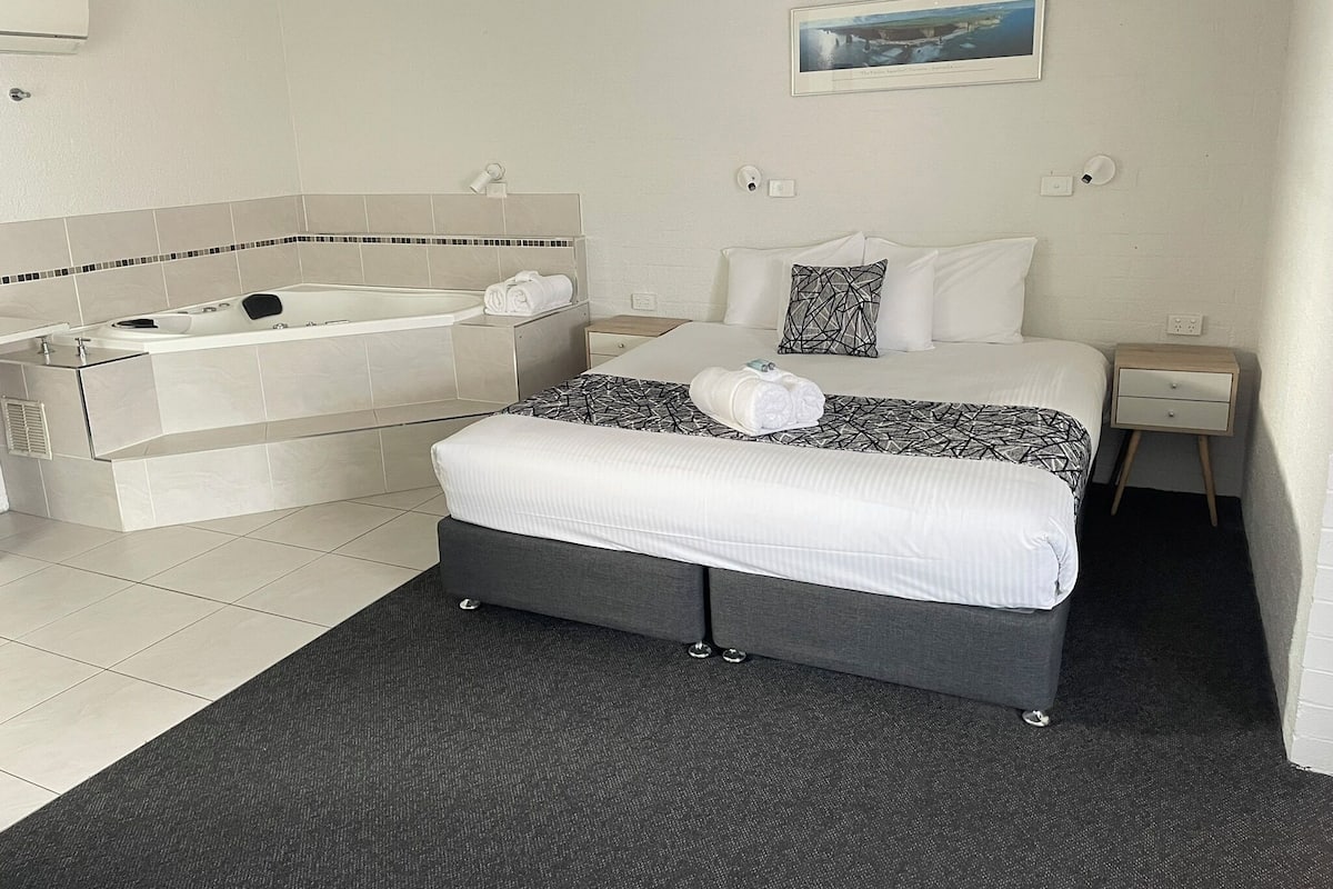 A hotel room with a large bed, a separate bathtub, a small bedside table, a nightstand, and a picture on the wall.