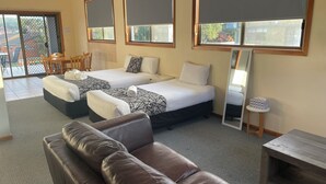 Habitación de hotel con dos camas, un sofá de cuero marrón, una mesita pequeña y un espejo grande.