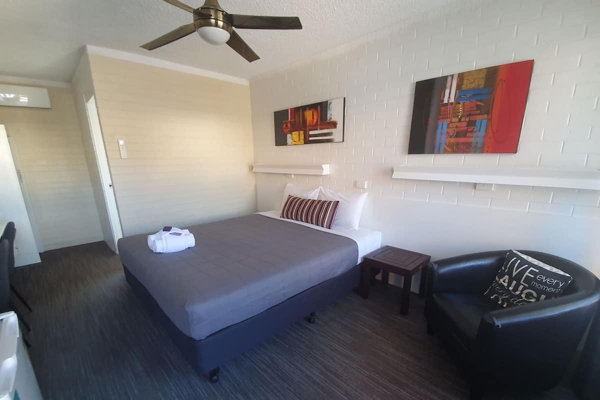 A hotel room with a bed, a chair, a small table, and artwork on the walls.