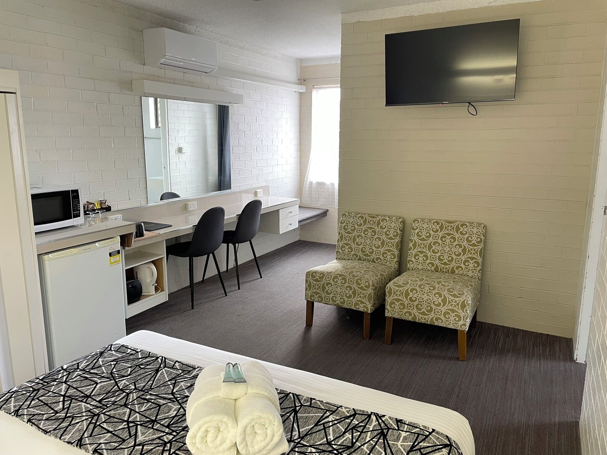 A hotel room with a bed, a desk with a chair, a TV, and a minibar.