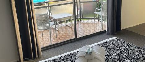A hotel room with a bed, a view of the outdoor area, and a balcony with chairs and a table.