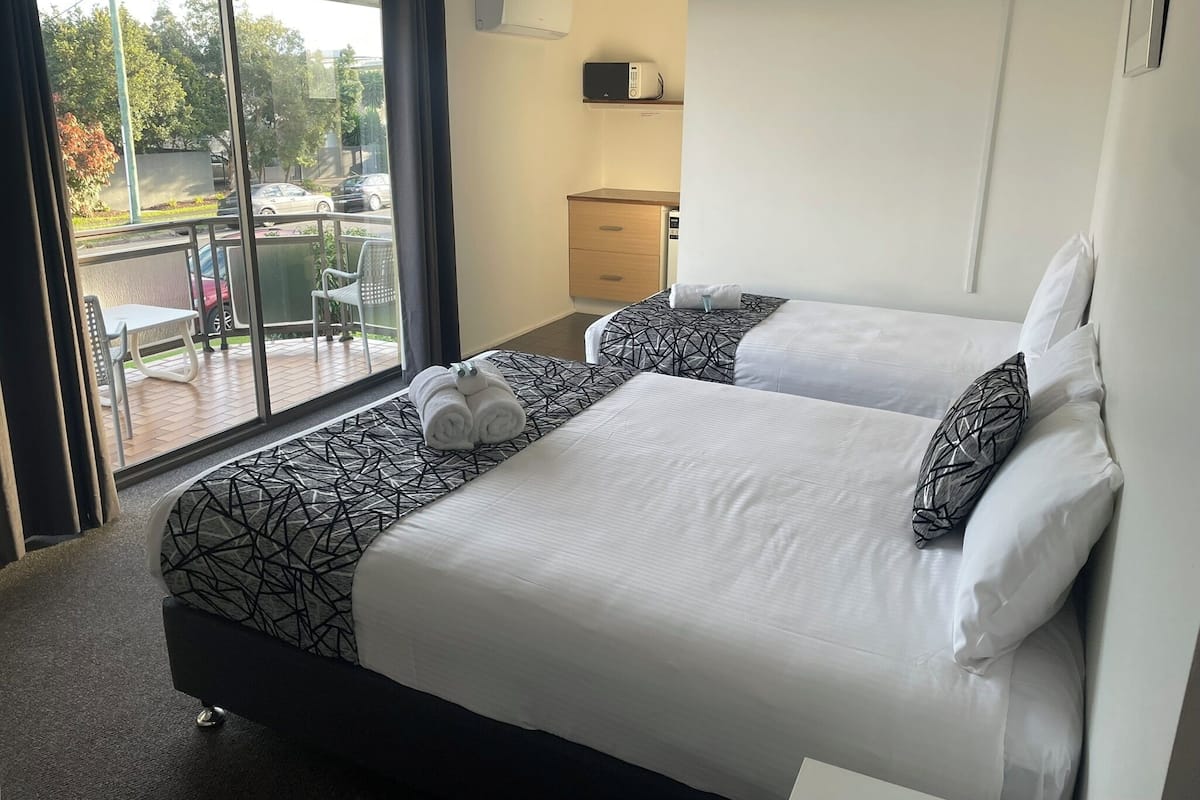 A hotel room with two beds, a balcony with a table and chairs, and a view of the outside.
