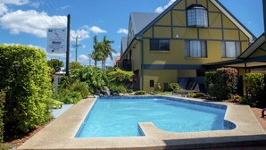 Un motel con piscina, rodeado de follaje y un cielo azul despejado.