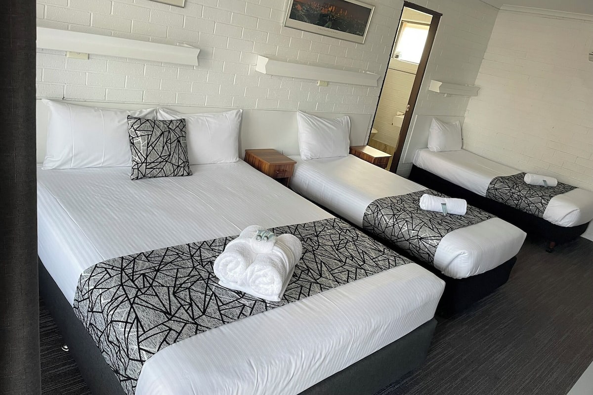 A hotel room with two beds, each with a geometric patterned bedspread, white pillows, and a towel on the bed. There is a wooden nightstand between the beds, a mirror on the wall, and a ceiling fan.