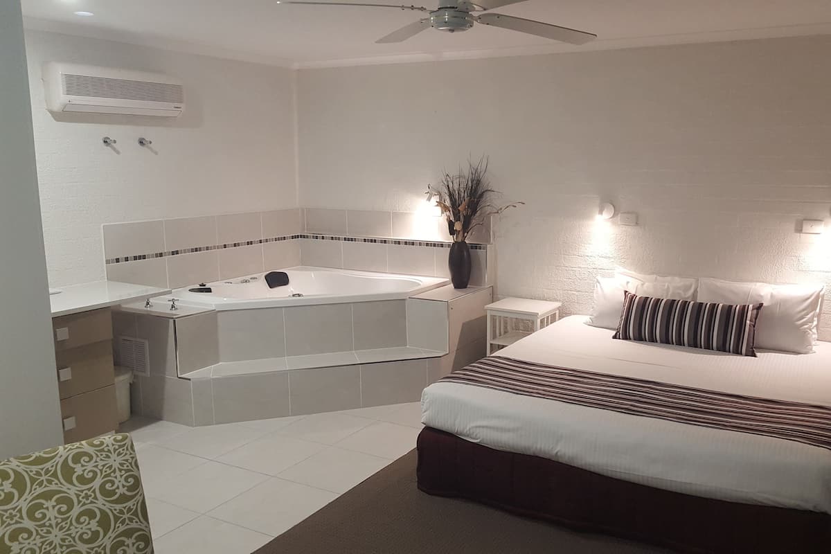 A hotel room with a large bed, a separate bathtub, a ceiling fan, and a small table.