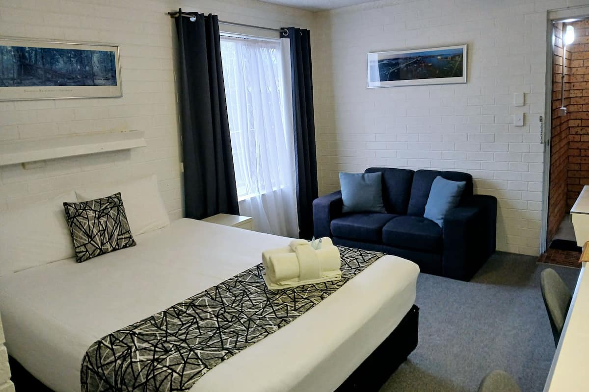 A hotel room with a bed, a sofa, a ceiling fan, and two framed pictures on the walls.