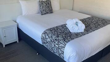 A neatly made bed with white linens and a geometric-patterned throw, a small bedside table, and a framed picture on the wall.
