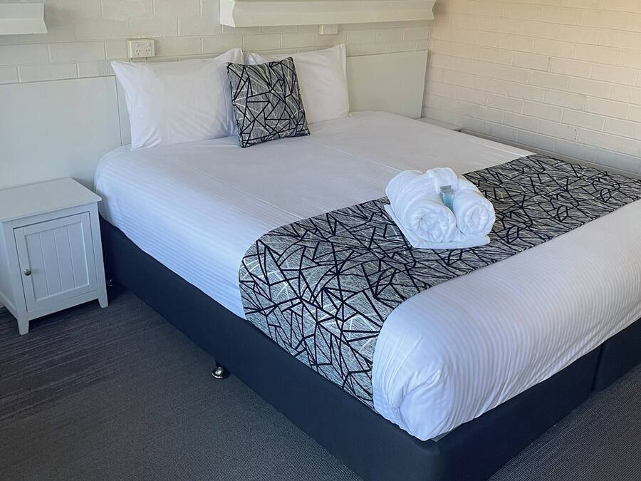 A neatly made bed with white linens and a geometric-patterned throw, a small bedside table, and a framed picture on the wall.