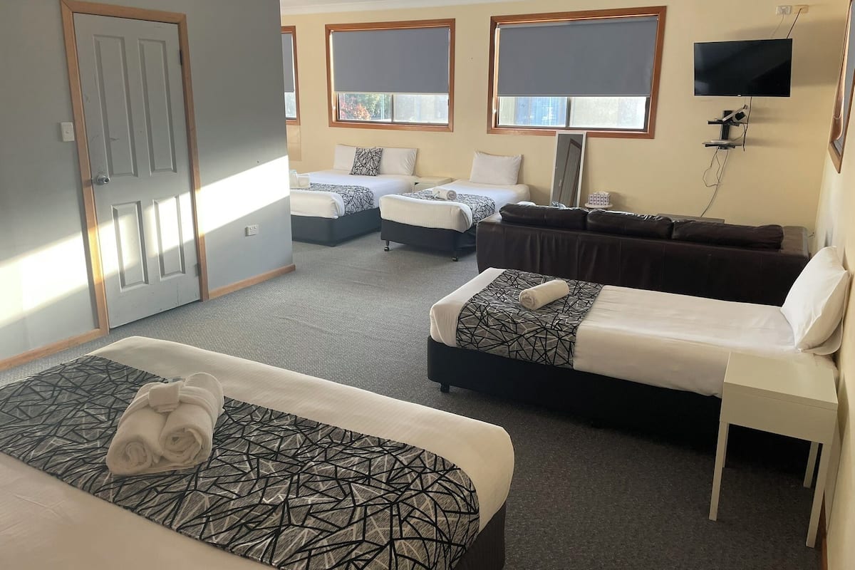 A hotel room with two beds, a sofa, a TV, and large windows.