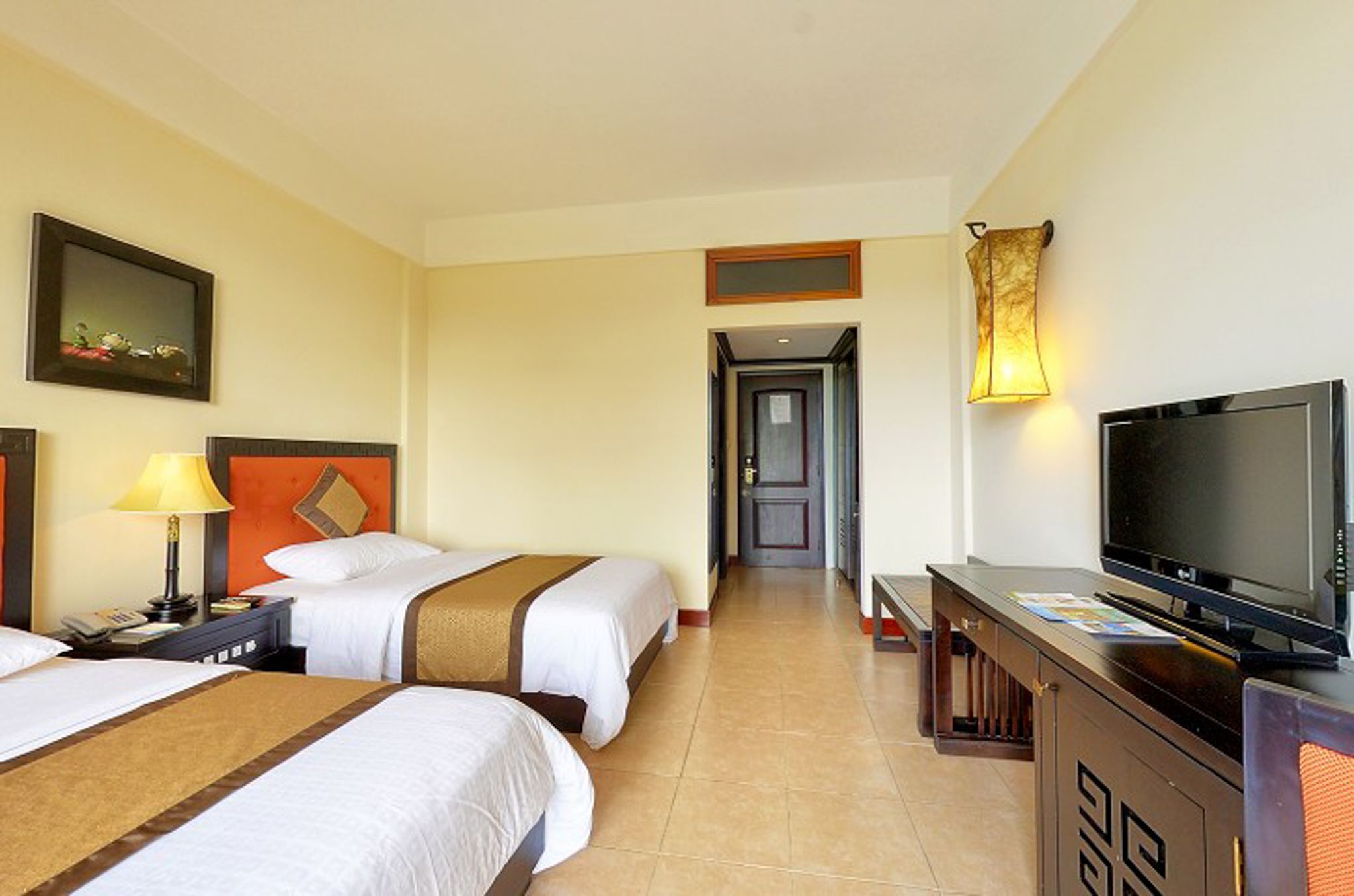 A hotel room with two beds, a TV, a desk, and a lamp.