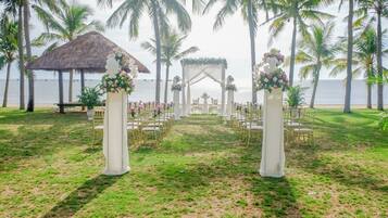 An outdoor wedding venue with a thatched structure, white floral decorations, and a view of the ocean.