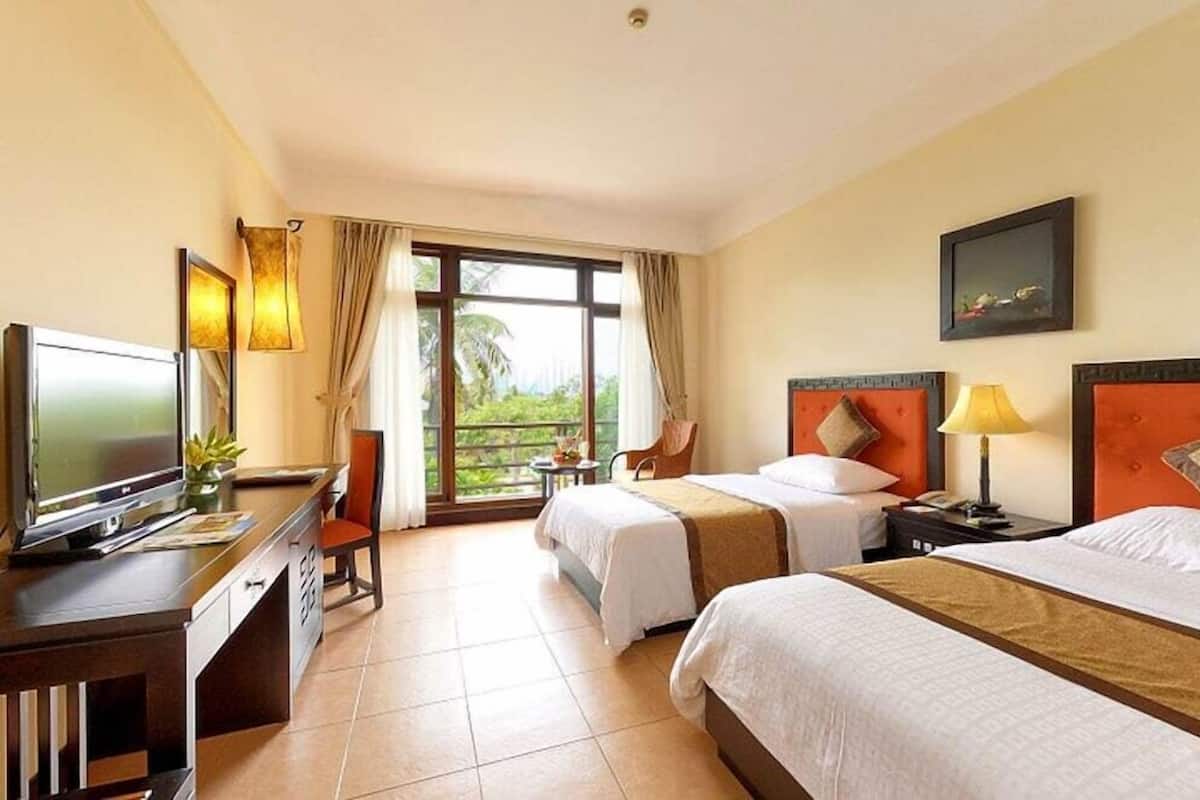 Habitación de hotel con dos camas, un escritorio con televisor, una silla, una mesita y una ventana con cortinas.