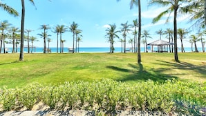 A beach with palm trees, a grassy area, and a gazebo. - Sun Spa Resort & Villas (Dong Hoi)