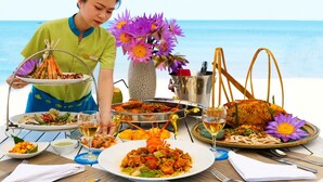 A table set with various dishes and a bottle of wine, a vase with purple flowers, and a person in a green uniform. - Sun Spa Resort & Villas (Dong Hoi)