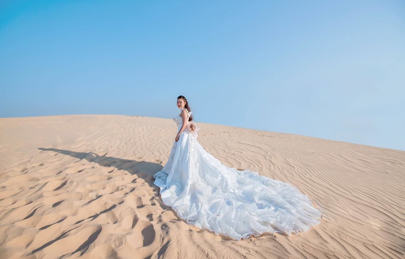 Una persona vestida de blanco parada sobre una duna de arena.