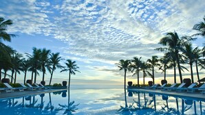 A poolside area with lounge chairs and palm trees, reflecting the sky and water. - Sun Spa Resort & Villas (Dong Hoi)