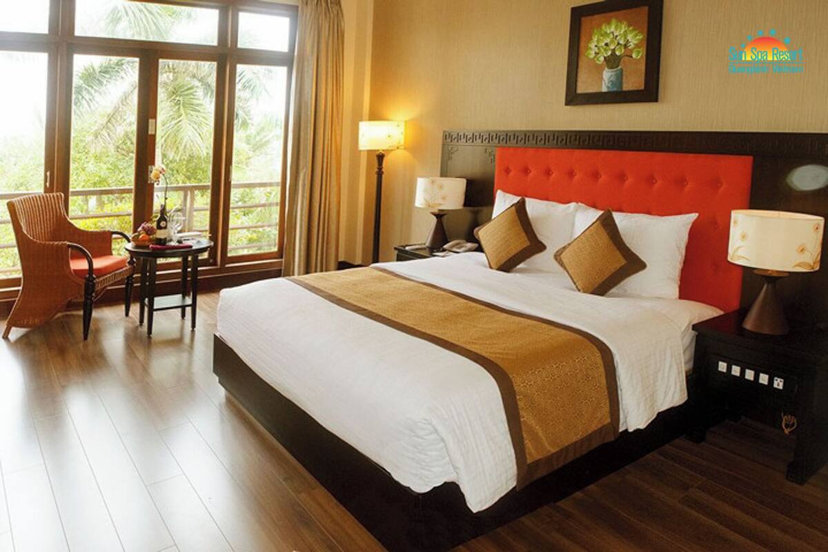 Una habitación de hotel con una cama grande, una silla, una mesita pequeña y una mesita de noche con lámpara.