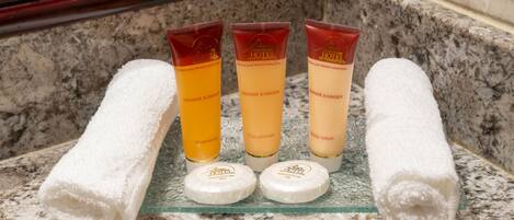 A bathroom counter with three toiletries: shampoo, conditioner, and body lotion, and two rolled towels.