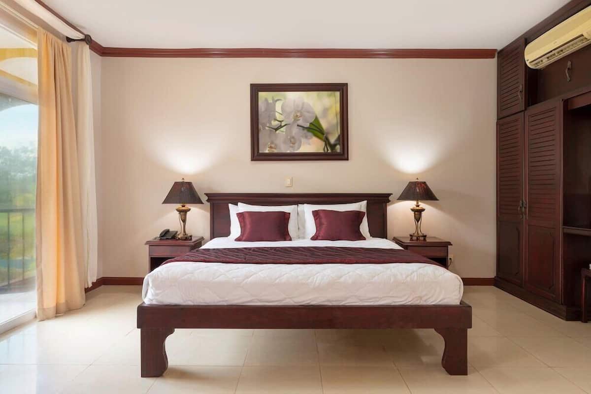 Una habitación de hotel con una cama grande, dos mesitas de noche con lámparas, un cuadro sobre la cama y un armario.