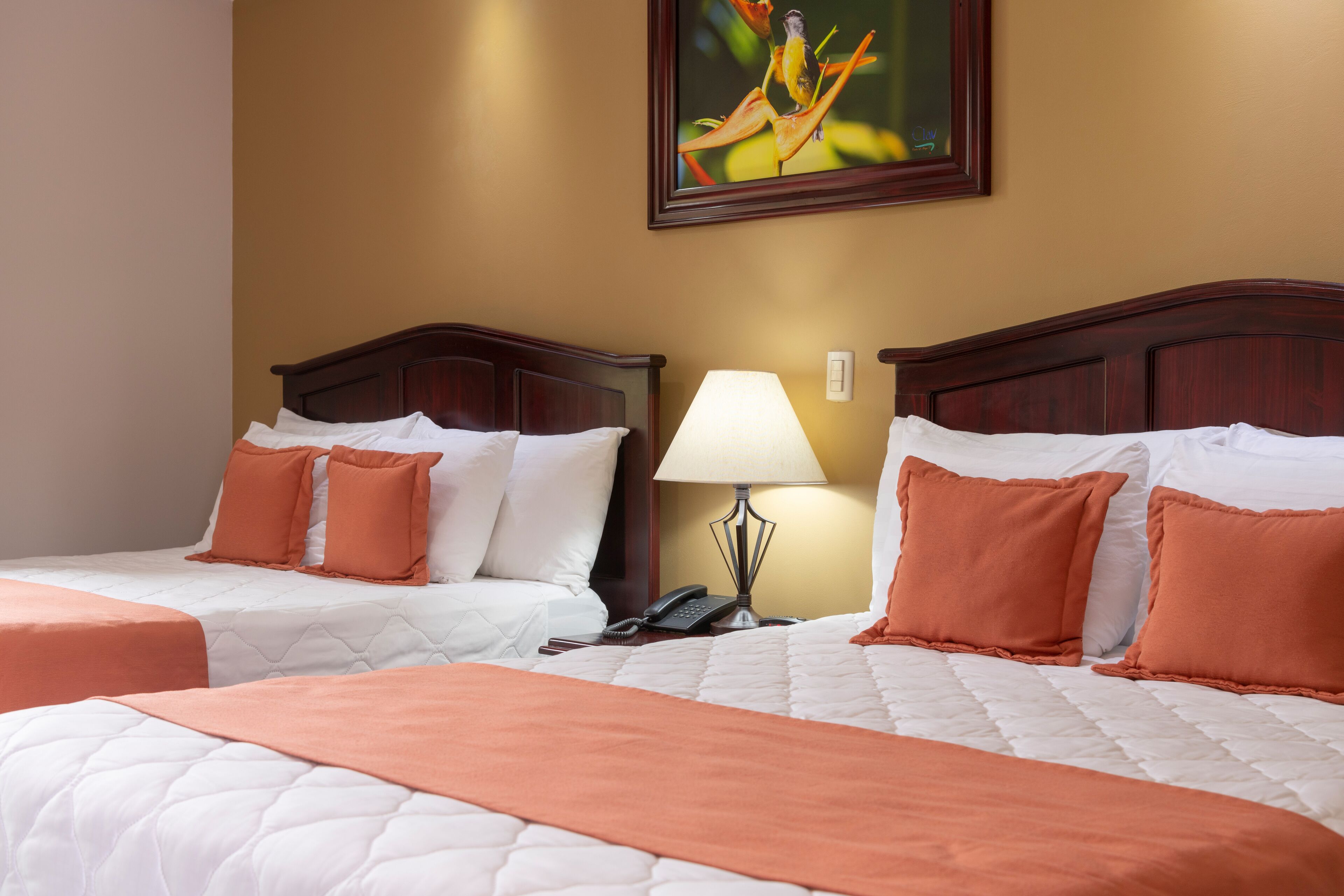 A hotel room with two beds, each with white and orange bedding, a bedside lamp, and a painting on the wall.