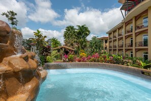 A hotel with a pool, palm trees, and a waterfall feature. - Hotel Magic Mountain SPA & Conference center (La Fortuna)