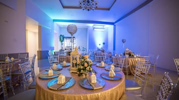 Un salón de banquetes con mesas redondas, sillas traslúcidas y una araña de cristal.