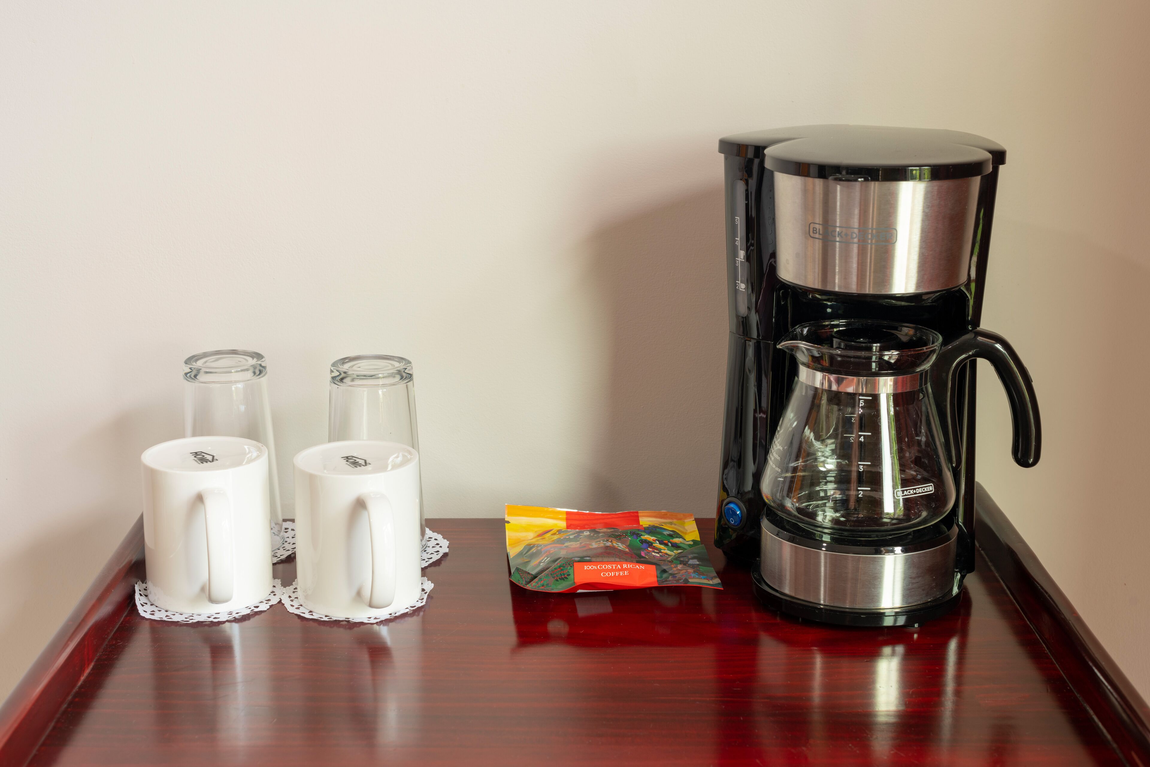 A coffee maker, two glass mugs, and a packet of biscotti on a wooden table.