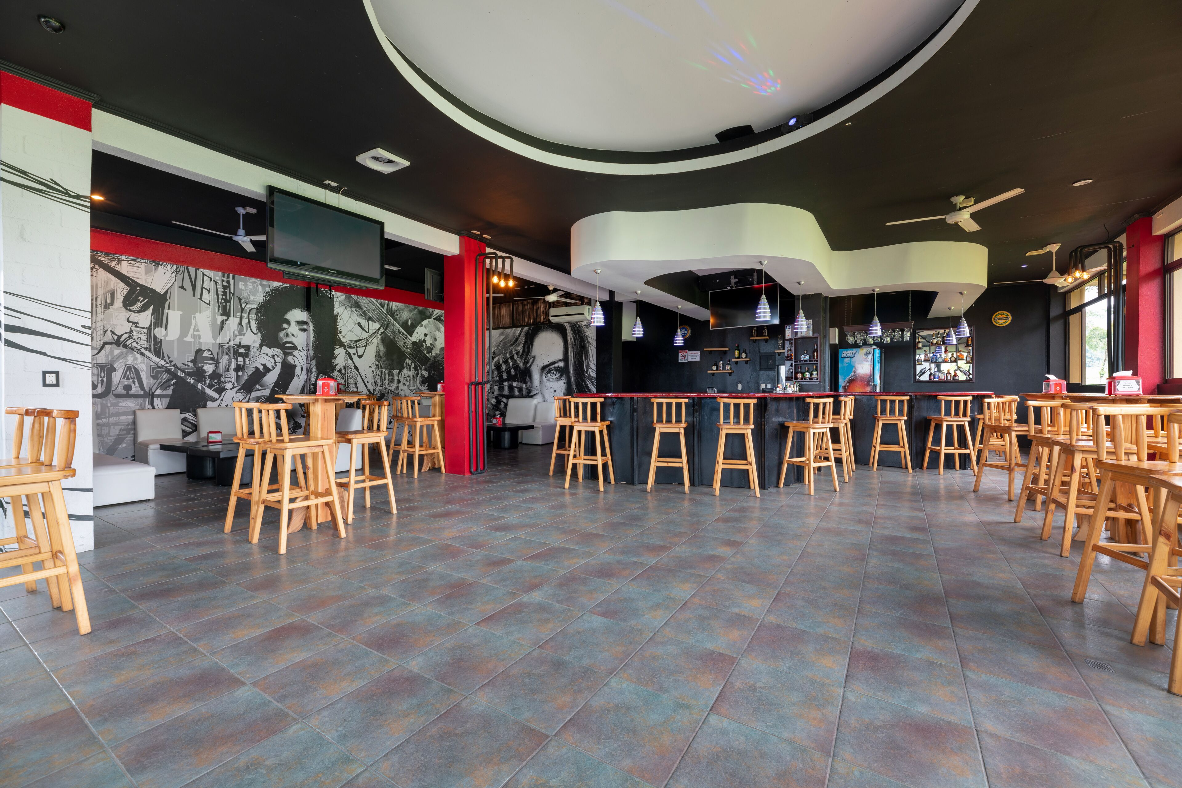 A spacious bar area with multiple wooden tables and chairs, a modern ceiling design, and a large mural on the wall.