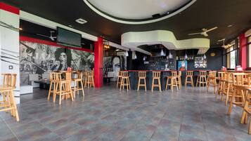 A spacious bar area with multiple wooden tables and chairs, a modern ceiling design, and a large mural on the wall.