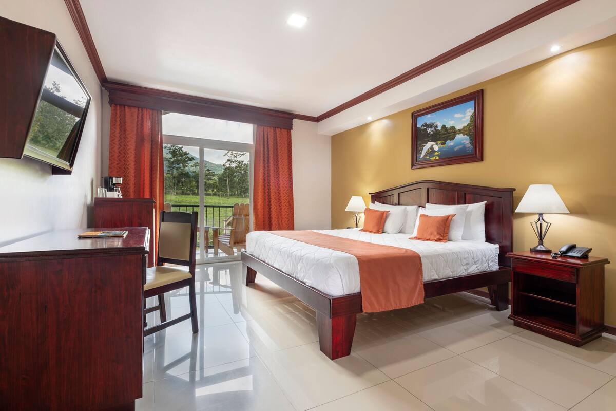 Habitación de hotel con cama, escritorio, silla, mesita de noche y televisor montado en la pared.