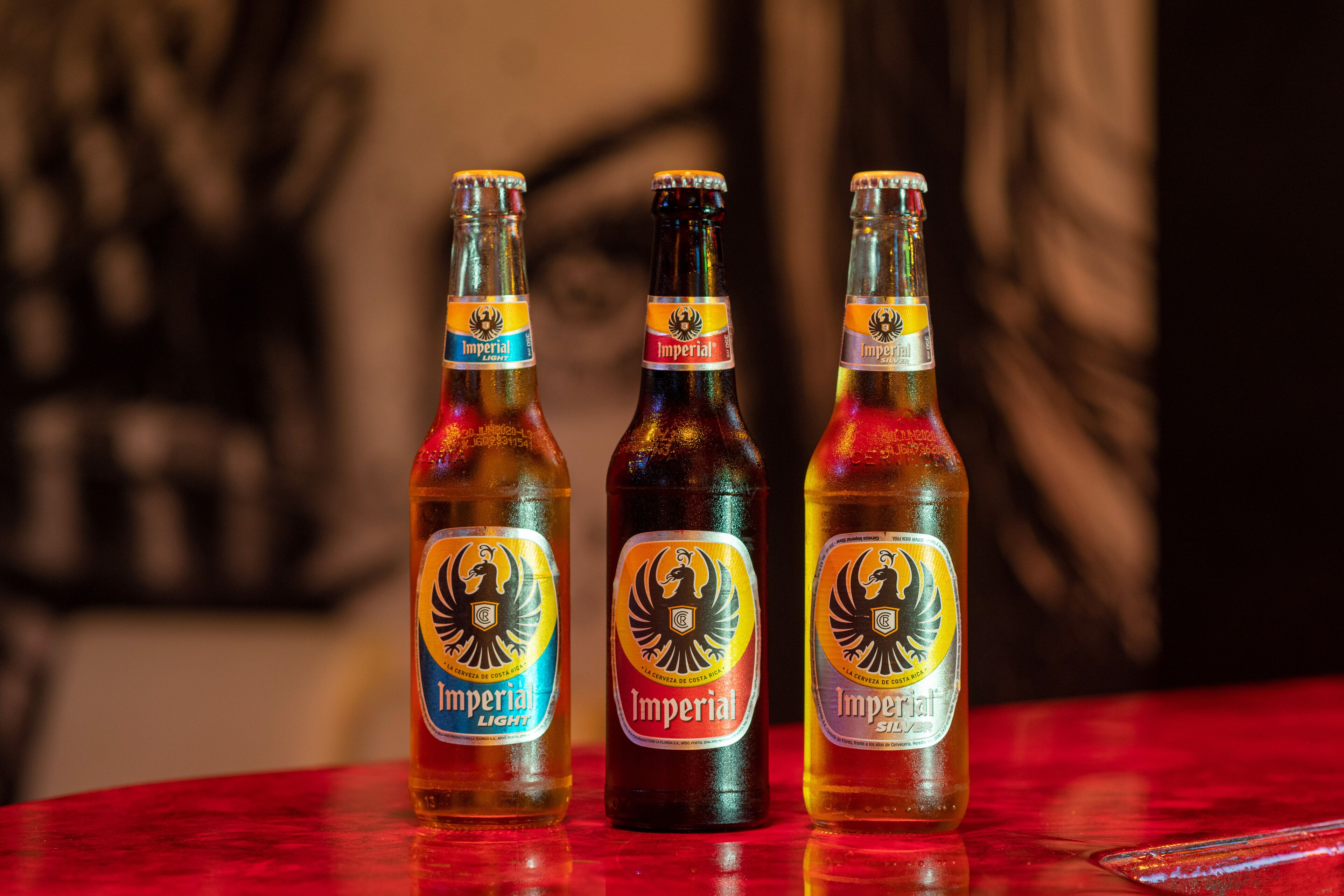 Trois bouteilles de bière, avec leurs étiquettes, posées sur une table rouge.