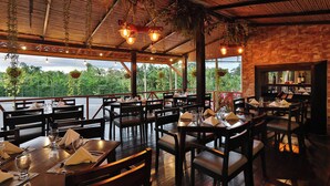 An outdoor restaurant with wooden tables and chairs, hanging plants, and a stone wall. - Hotel Magic Mountain SPA & Conference center (La Fortuna)