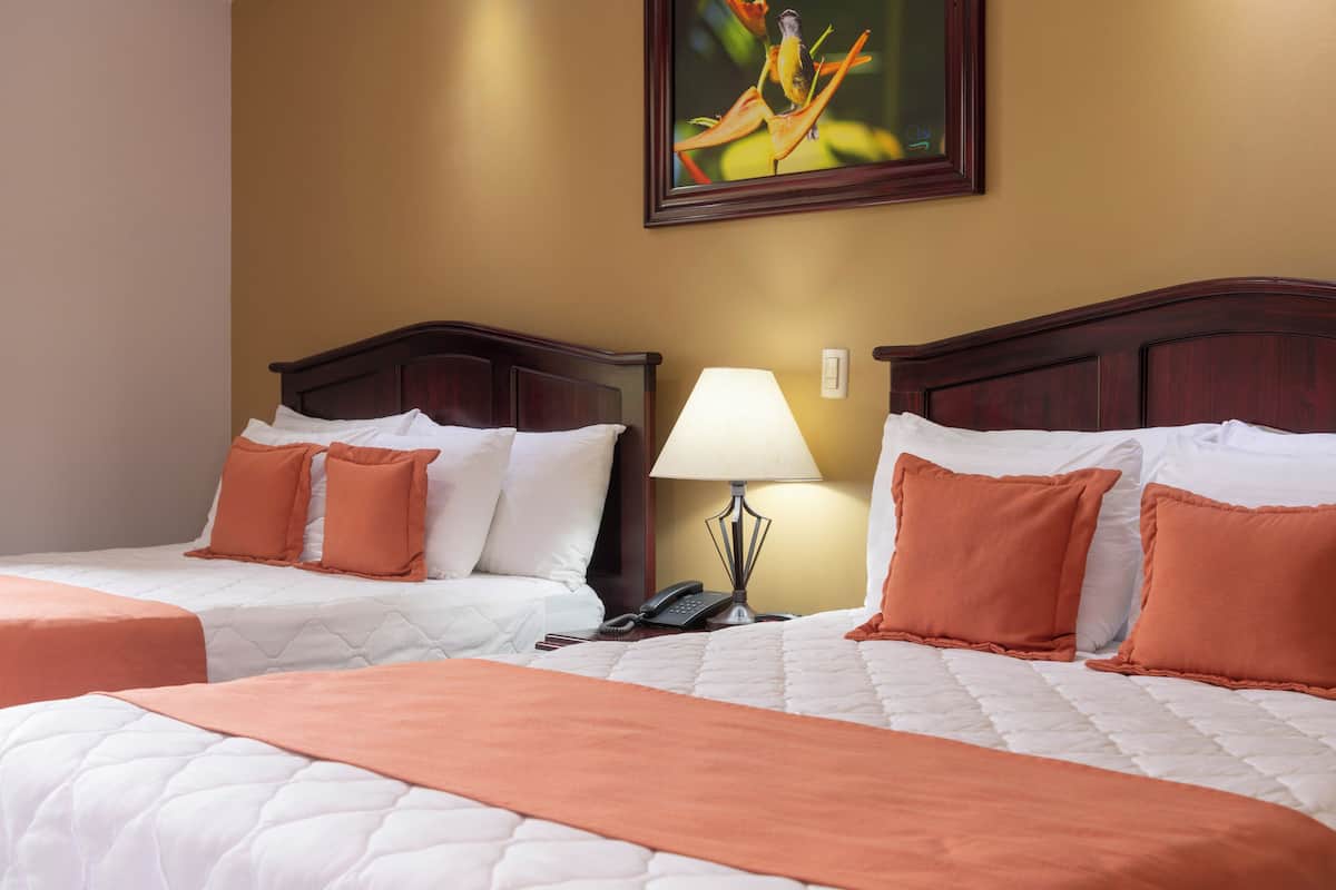 A hotel room with two beds, a nightstand with a lamp, and a painting on the wall.