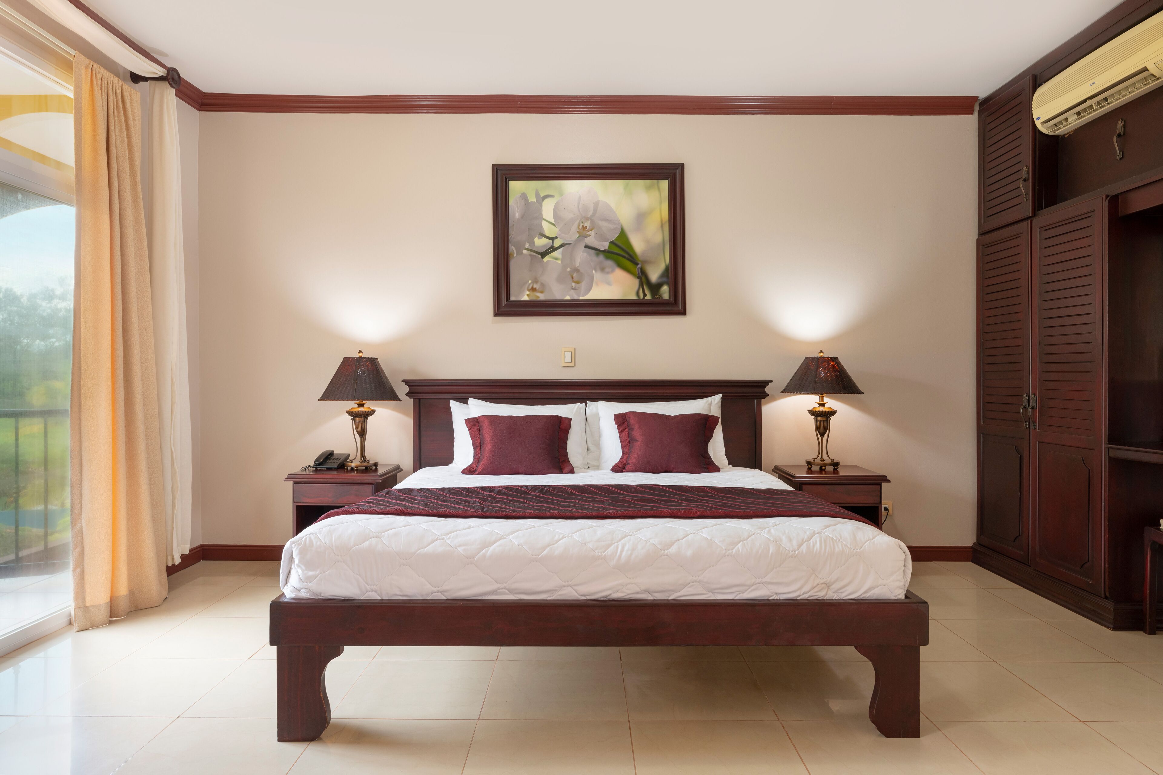 A large bed with a wooden frame, two bedside tables with lamps, a painting on the wall, and a wardrobe.