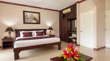 Habitación de hotel con una cama grande, dos lámparas de noche, una mesita de noche, un cabecero de madera, un calentador de pared, una puerta y una mesa con un arreglo floral.