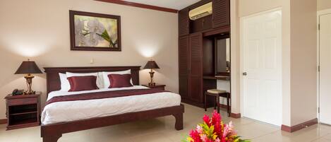 Une chambre d’hôtel avec un grand lit, deux lampes de chevet, une table de chevet, une tête de lit en bois, un radiateur fixé au mur, une porte et une table agrémentée d’un arrangement floral.