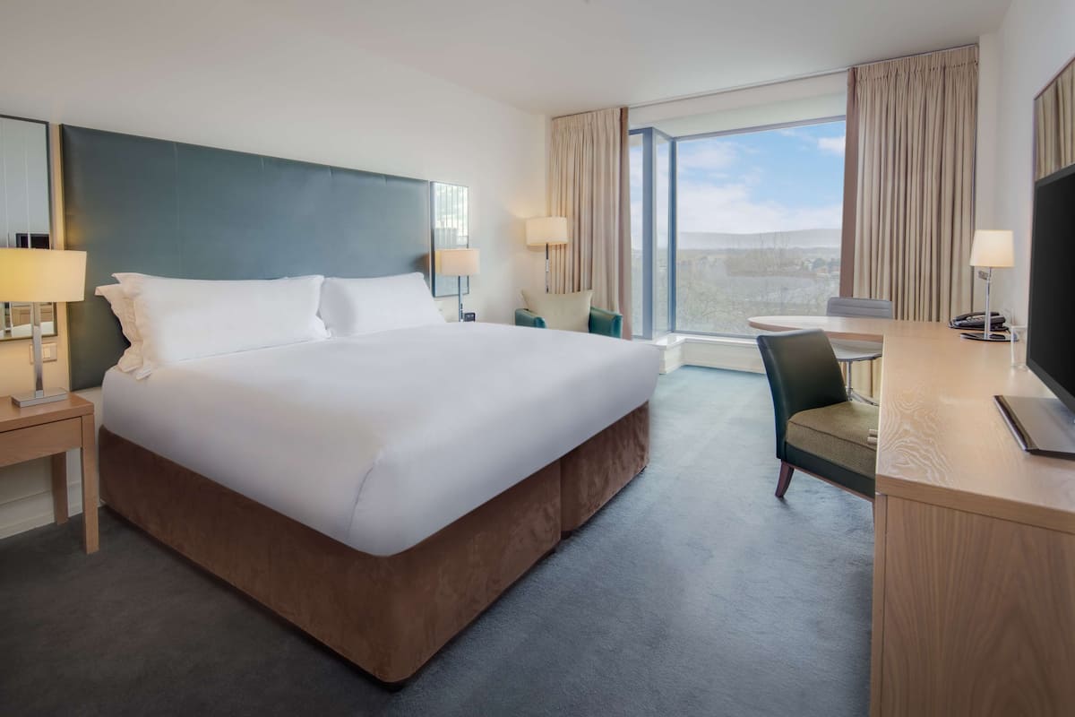 A hotel room with a large bed, a desk with a chair, a TV, and a window with curtains.