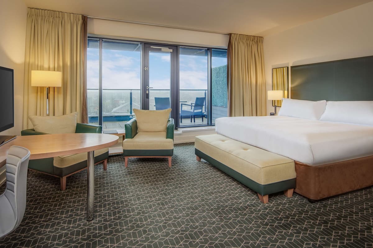 A hotel room with a bed, a desk, a chair, a small table, and a balcony with chairs.