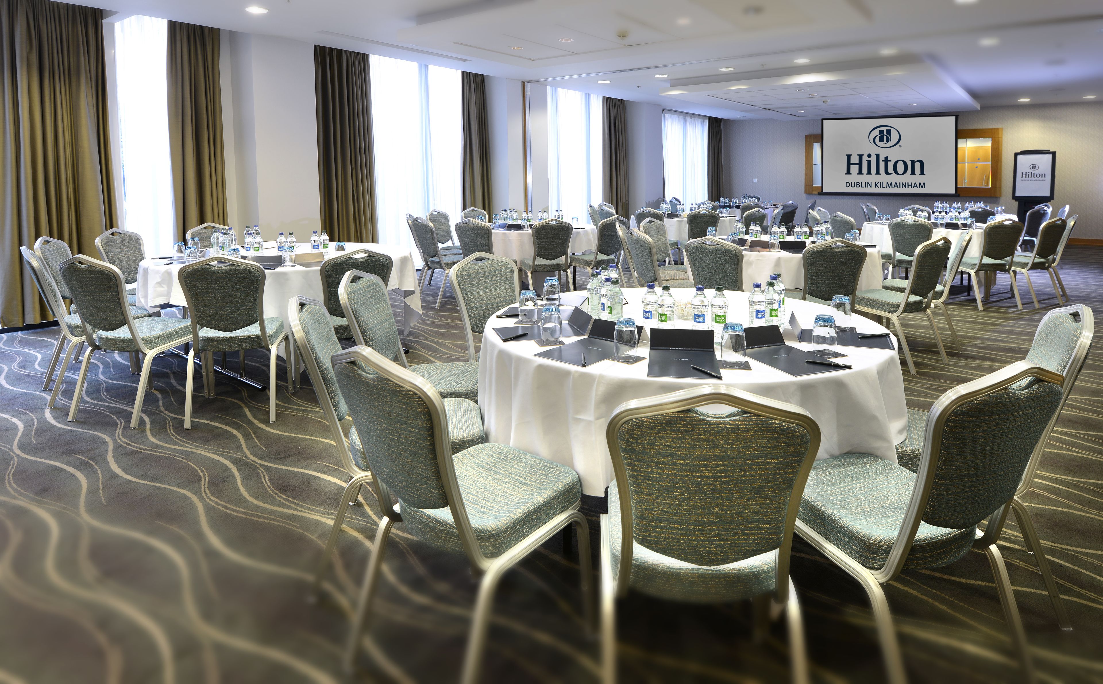 A conference room at the Hilton Dublin Kildare with round tables, chairs, and water bottles.
