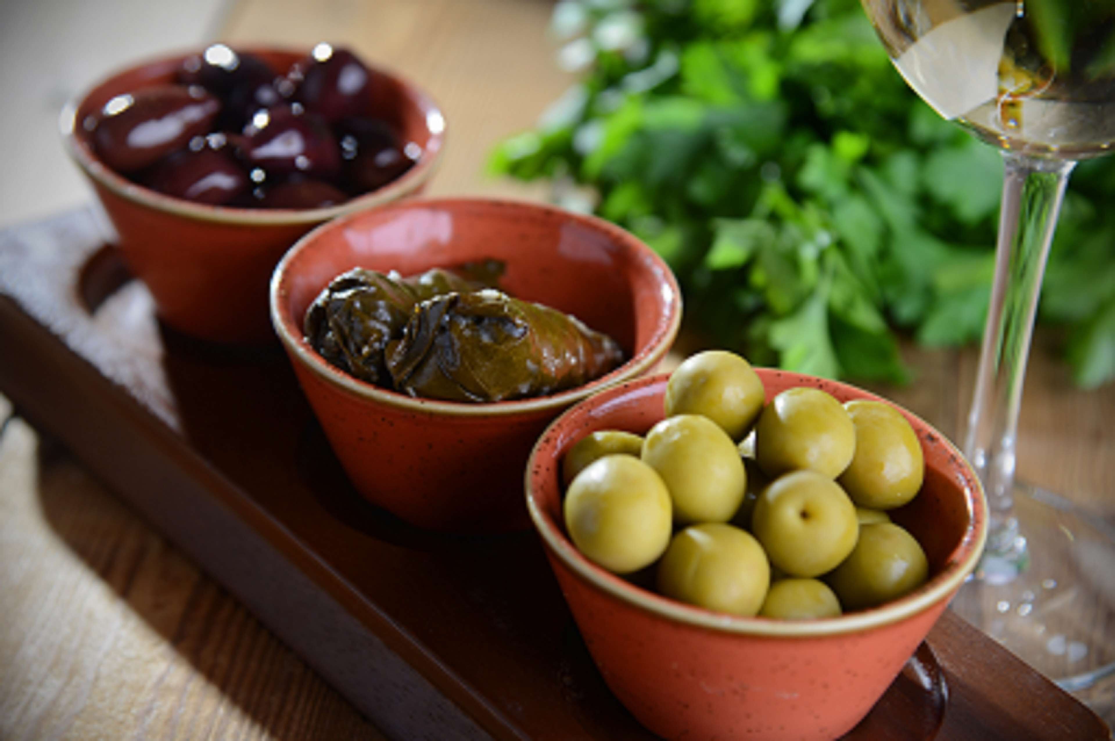Three bowls of olives and a glass of wine on a wooden table.