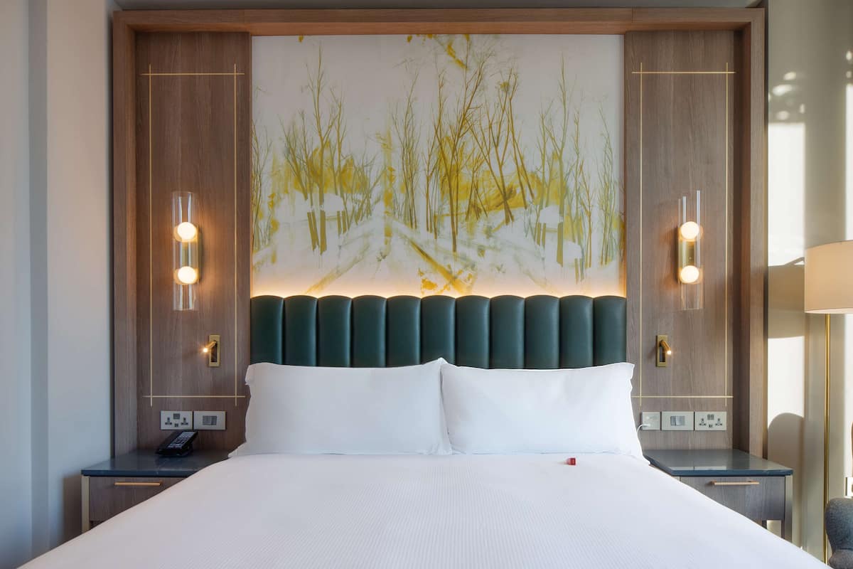 A hotel room with a large bed, a headboard with a painting, bedside lamps, and a nightstand with a phone.