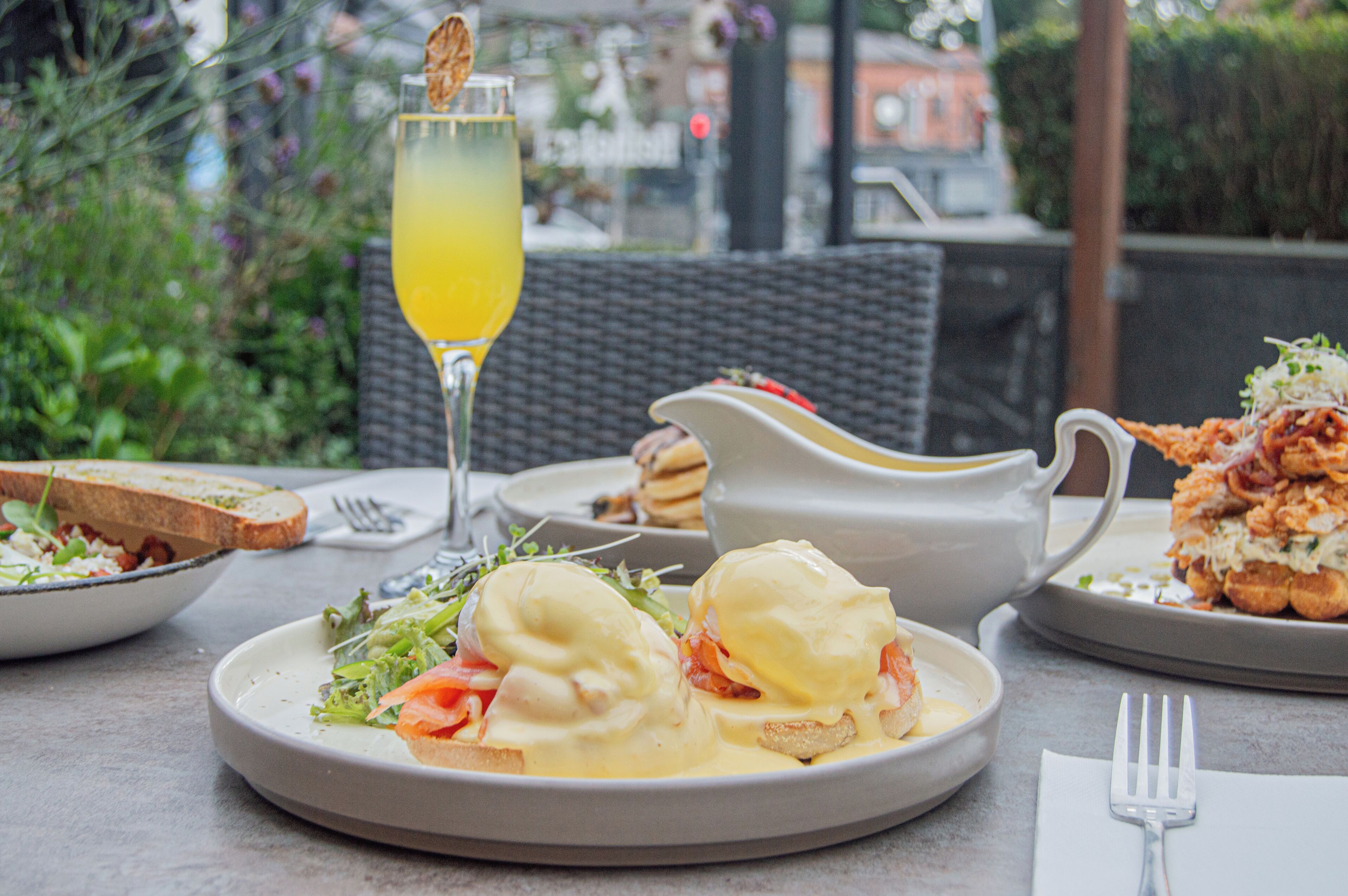 A table with a plate of eggs benedict, a glass of orange juice, and a pitcher of sauce.