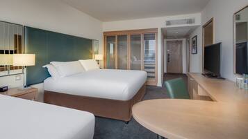 A hotel room with a large bed, a desk with a flat-screen TV, a mirror, and a walk-in closet with sliding doors.